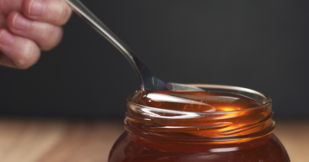 spoon in glass jar full of honey, wide photoの写真素材