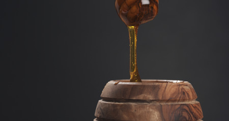 honey drips from dipper in pot, wide photoの写真素材