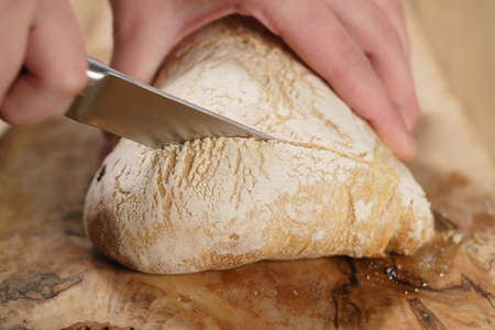 closeup man slicing ciabatta on wood board, shallow focusの写真素材