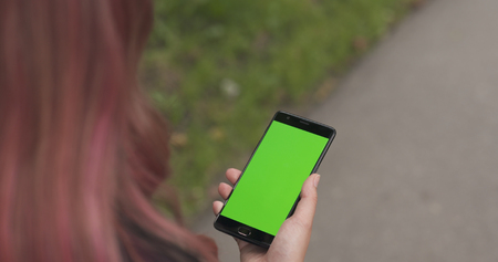 female teen holding smartphone with green screen on sidewalk in townの写真素材