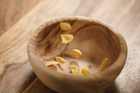 corn flakes falling into wood bowl closeup, shallow focusの写真素材