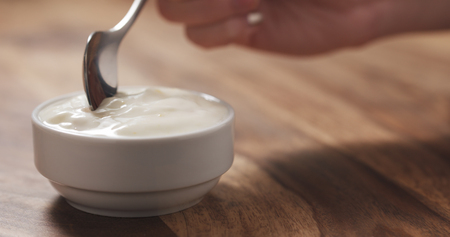 young female hand eating peach yogurt with spoonの写真素材