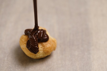 pouring dark chocolate on profiterole on parchment paper