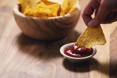young female hand dipping nachos in tomato salsa sauce, shallow focus
