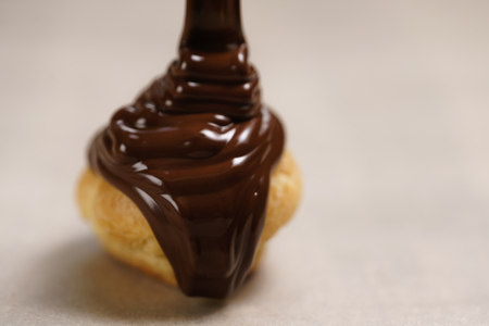 pouring dark chocolate on profiterole on parchment paper