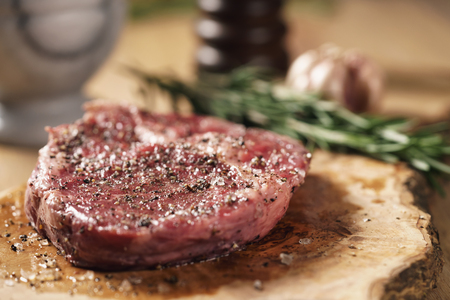 fresh raw rib eye steak in spices on wood board on kitchen tableの写真素材