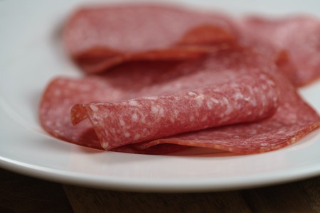 sliced salami on white plate on wood table