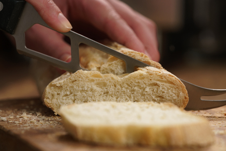 Young female hands slicing fresh baguette on cutting board closeupの写真素材