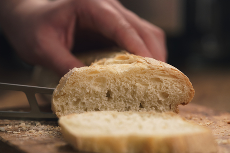 young female hands slicing fresh baguette on cutting board closeup