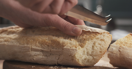 closeup slicing fresh baguette on cutting boardの写真素材