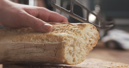 closeup slicing fresh baguette on cutting board