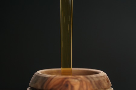 organic honey pour into wooden pot, closeup photo
