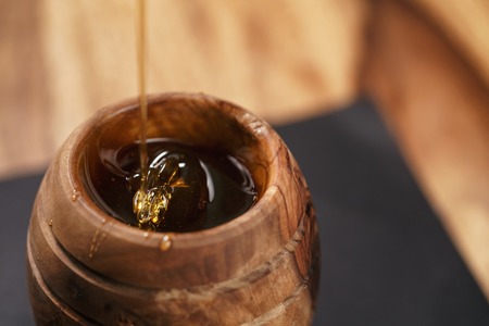 organic honey drips from wooden dipper in jar, closeup photoの写真素材