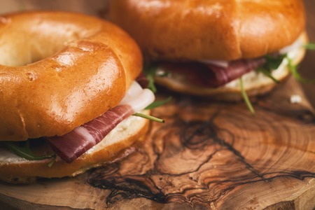 two bagels with prosciutto and cream cheese on wood boarの写真素材