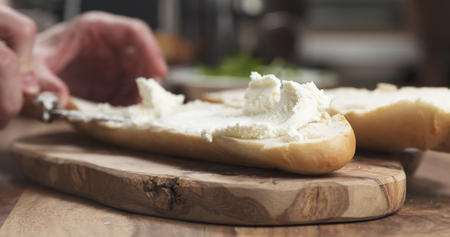 spreading cream cheese on baguette on wood boardの写真素材