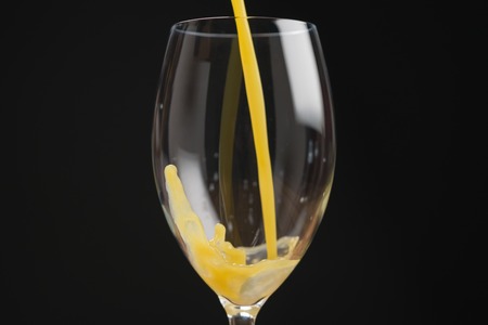 pouring orange juice into glass over black backgroundの写真素材