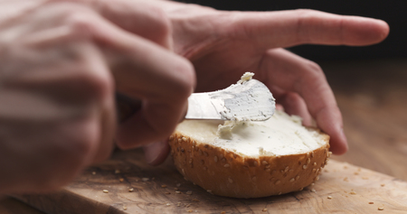 man hands spreading cream cheese on sesame bun on wood boardの写真素材