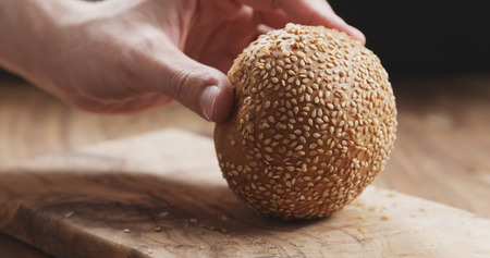 closeup man cuts sesame bun on wood boardの写真素材