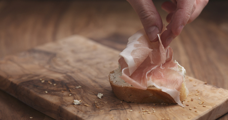 making prosciutto on baguette slice with cream cheese on wood boardの写真素材