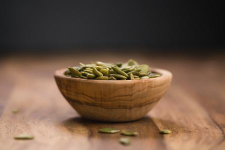 green pumkin seeds in bowl on wooden tableの写真素材