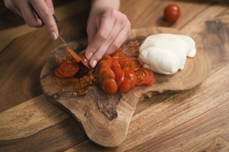female teen hand slicing cherry tomatoes with knife on wooden boardの写真素材