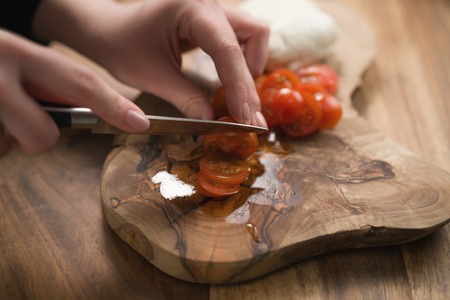 female teen hand slicing cherry tomatoes with knife on wooden boardの写真素材