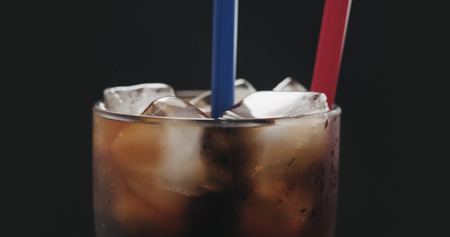 two straws in cola with ice cubes in glass over black backgroundの写真素材