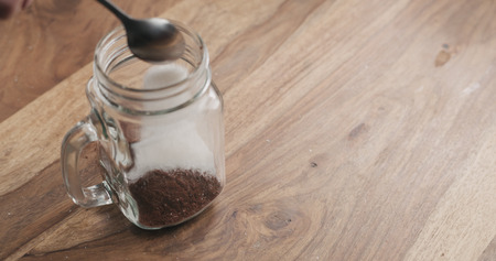 making cocoa drink in glass jar with handle on wood table, adding sugarの写真素材