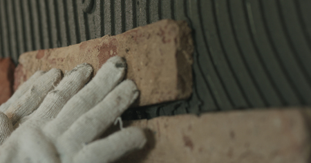closeup worker applying brick cuts tile to the wall