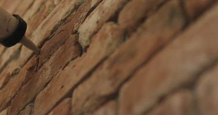 Slow motion closeup of worker filling seam between bricks with mortar from sealant gun