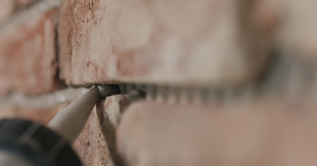 Slow motion closeup of worker filling seam between bricks with mortar from sealant gunの写真素材