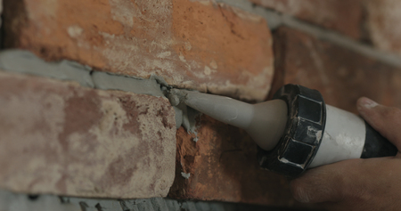 Slow motion closeup of worker filling seam between bricks with mortar from sealant gunの写真素材