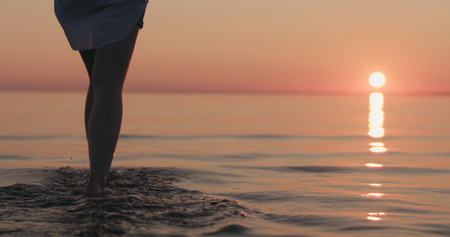 closeup young female legs walking in shallow water on a beachの写真素材