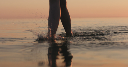closeup young female legs walking in shallow water on a beachの写真素材