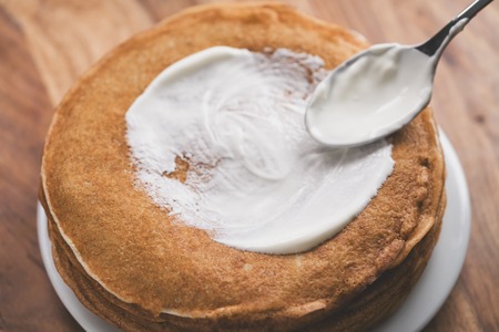 Adiing sour cream to stack of fresh hot crepes or blinis on wood tableの写真素材