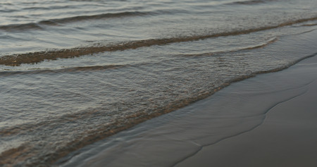Closeup of small waves on a beach at sunset, wide photo