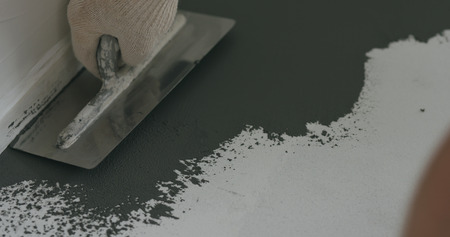 closeup male worker applying micro concrete plaster coating on the floor with a trowel