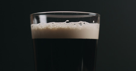 Closeup dark beer with bubbles over black background