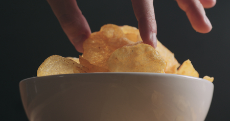 closeup man hand taking potato chip from white bowl low angle shot, wide photoの写真素材