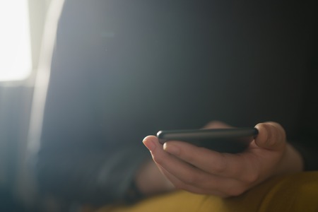 Closeup young female using smartphone sitting indoors near windowの写真素材