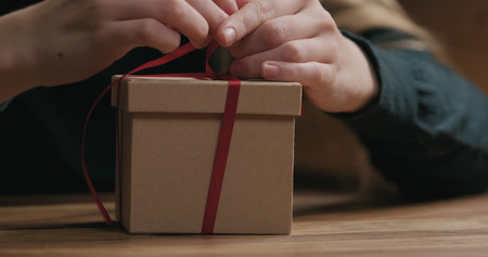 Closeup shot of female hands tying red ribbon bow on craft paper gift boxの写真素材