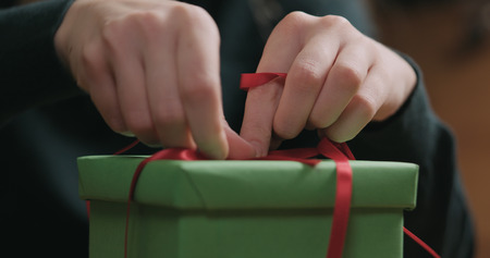 Closeup shot of female hands tying red ribbon bow on green paper gift boxの写真素材