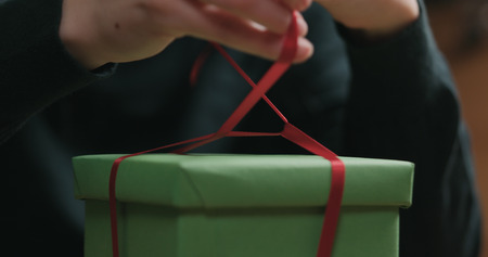Closeup shot of female hands tying red ribbon bow on green paper gift box