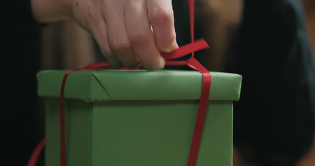 Closeup shot of female hands tying red ribbon bow on green paper gift boxの写真素材