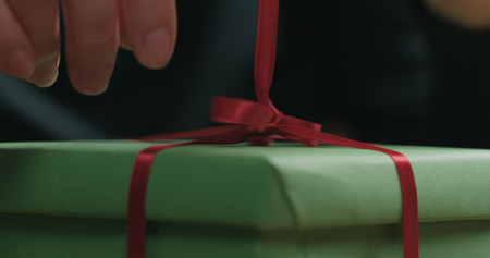 Macro shot of female hands tying red ribbon bow on green paper gift boxの写真素材