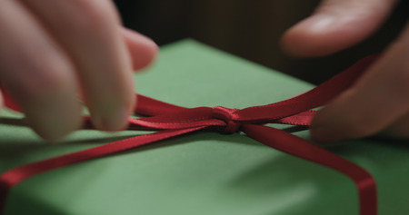 Macro shot of female hands tying red ribbon bow on green paper gift boxの写真素材