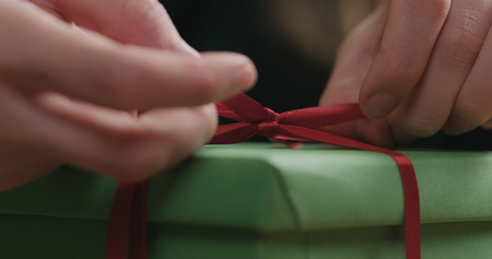 Macro shot of female hands tying red ribbon bow on green paper gift boxの写真素材