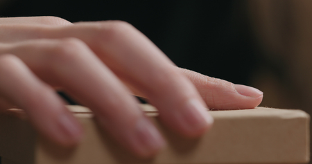 closeup shot of young female hands unties red ribbon bow on craft paper gift box, wide photoの写真素材