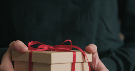 Closeup female hands shows gift box with red ribbon bow, wide photoの写真素材