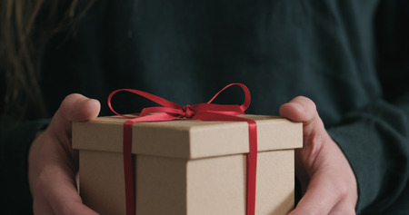 Closeup female hands shows gift box with red ribbon bow, wide photoの写真素材
